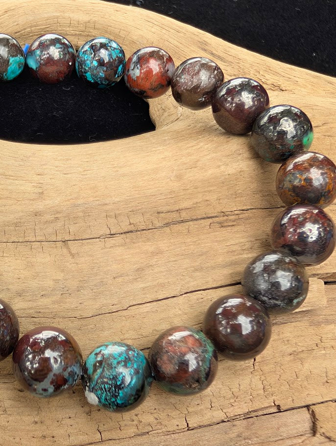 Macro close-up of 8mm polished Phoenix Stone beads highlighting the high-gloss finish and vibrant teal chrysocolla spots against a dark matrix.