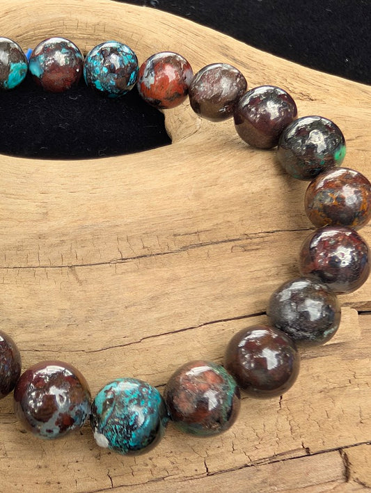 Macro close-up of 8mm polished Phoenix Stone beads highlighting the high-gloss finish and vibrant teal chrysocolla spots against a dark matrix.