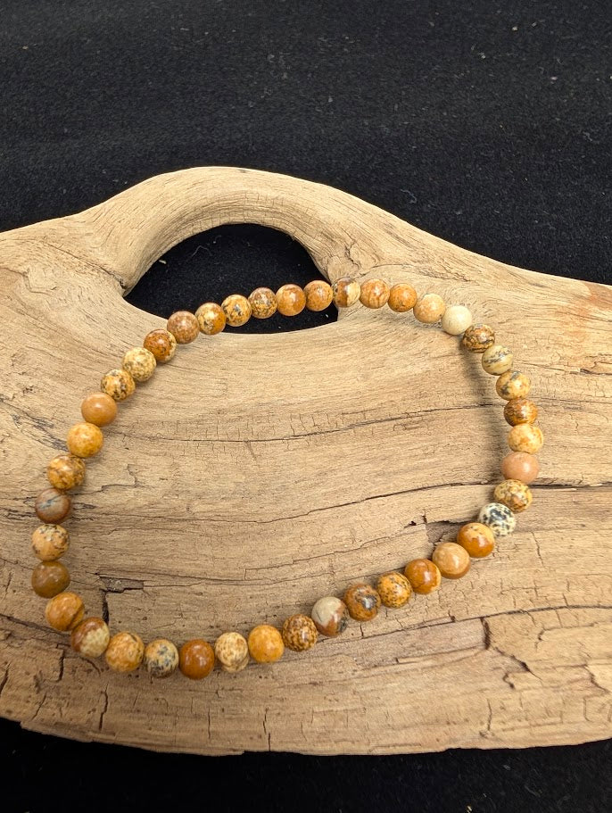 4mm smooth Picture Jasper beaded stretch bracelet resting on a driftwood display, showing warm tan and brown scenic patterns.