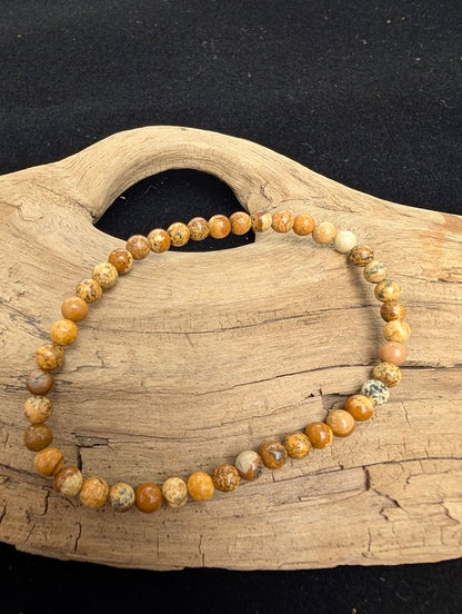 4mm smooth Picture Jasper beaded stretch bracelet resting on a driftwood display, showing warm tan and brown scenic patterns.