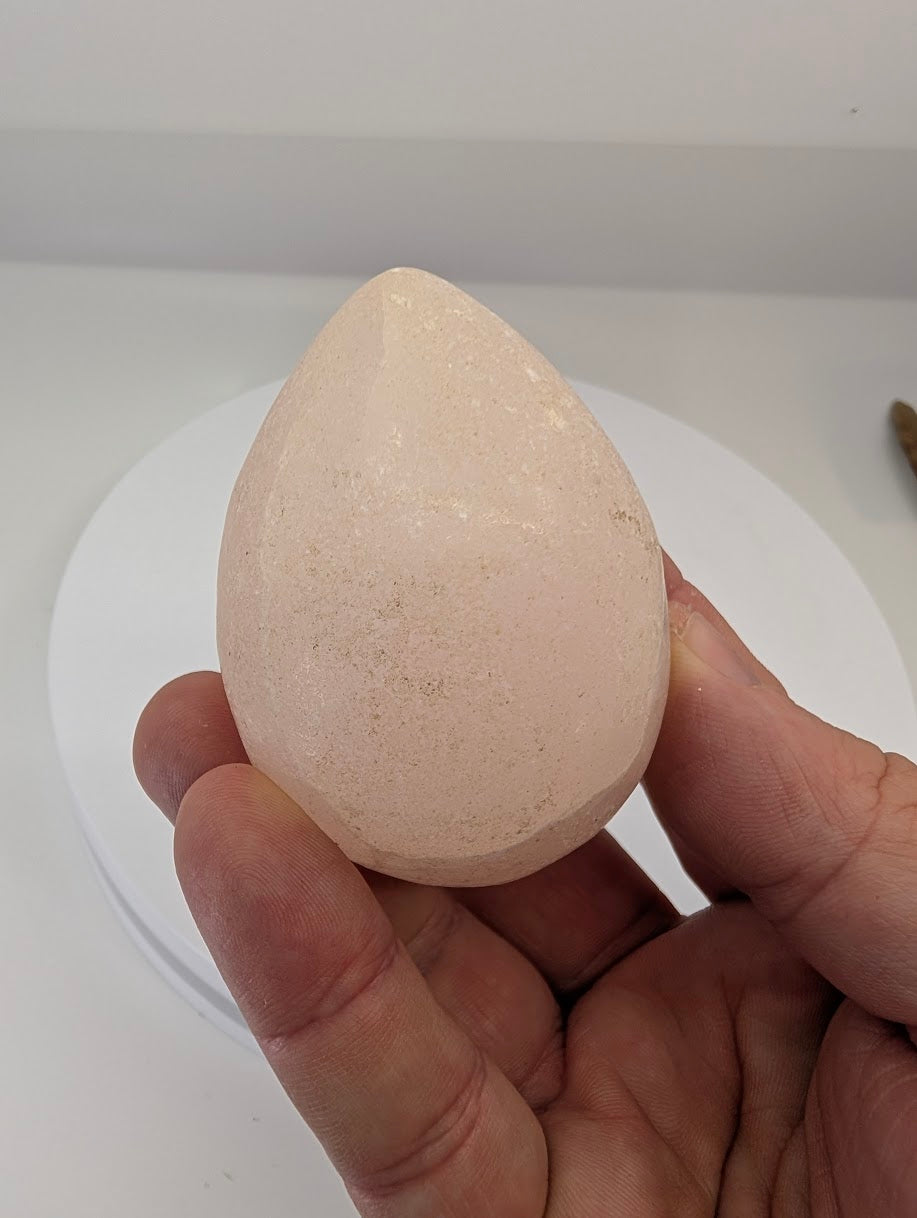 Hand-held view of a polished pink calcite egg showing natural texture and translucency