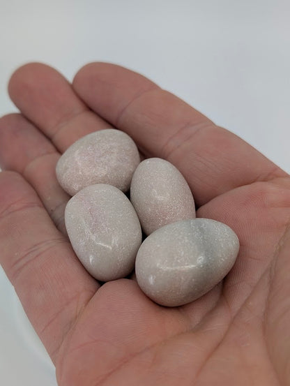 Pink Opal tumbled stones shown in hand for scale