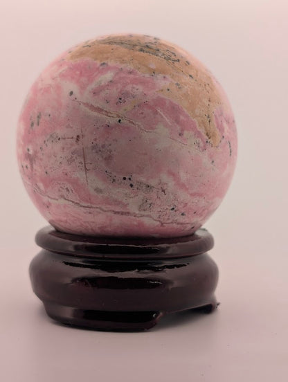 Side profile of Peruvian rhodonite sphere on dark wood stand