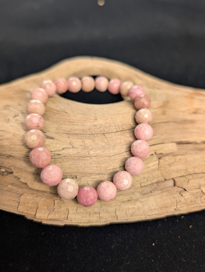 8mm faceted Pink Petrified Wood beaded stretch bracelet resting on a driftwood display, showing soft pastel pink colouration.