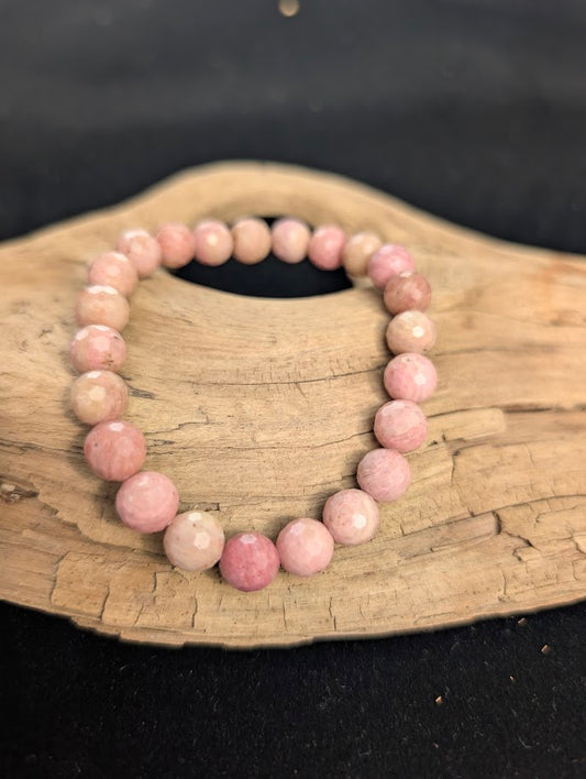8mm faceted Pink Petrified Wood beaded stretch bracelet resting on a driftwood display, showing soft pastel pink colouration.