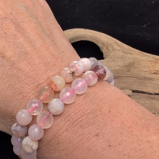 Video demonstrating the 8mm faceted Flower Agate beaded stretch bracelet in motion, highlighting the light-catching geometric cuts and the natural three-dimensional chalcedony blossom formations within the matrix, strung on a pink elastic cord.