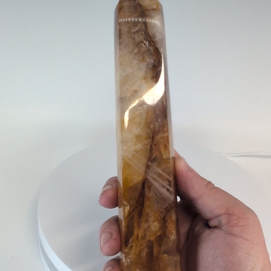 Brazilian Golden Healer Quartz Tower illuminated from behind — internal golden bands and translucent structure glowing through quartz under light.