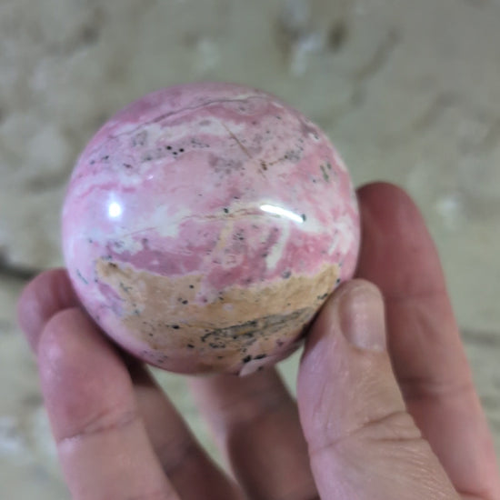 video of Polished rhodonite sphere close-up with black manganese inclusions