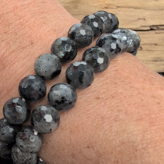 Video showcasing the highly reflective faceted texture, dark grey matrix, and brilliant silver-blue optical flash (schiller effect) of an 8mm Larvikite beaded stretch bracelet worn on a wrist.
