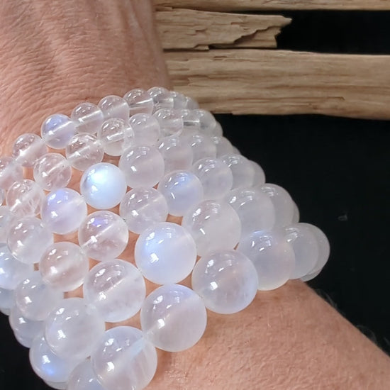 A wrist wearing multiple stacked Sri Lankan White Moonstone bracelets, rotating slowly to show the vivid blue adularescent flash moving across the high-clarity beads in natural light.