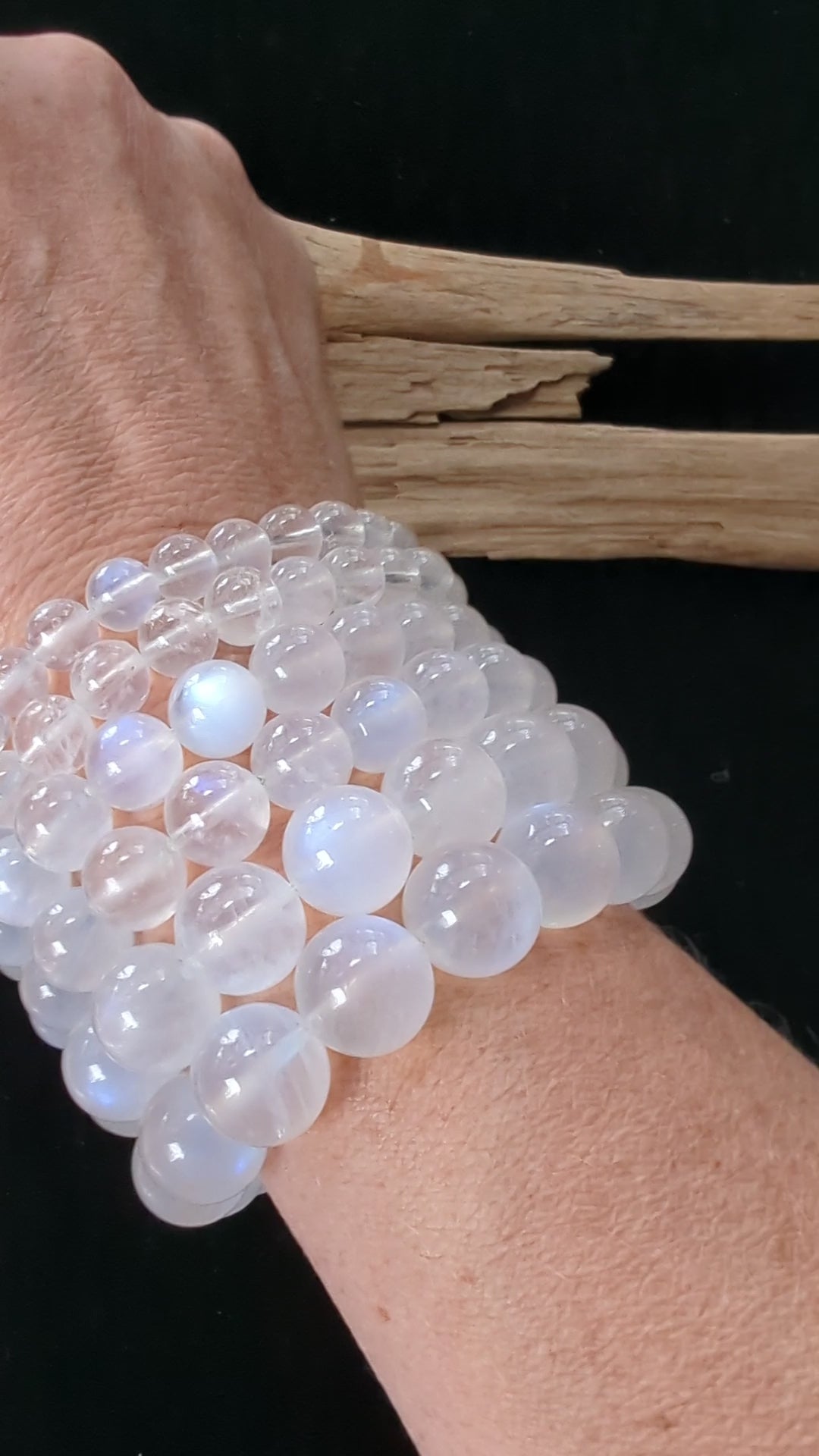 A wrist wearing multiple stacked Sri Lankan White Moonstone bracelets, rotating slowly to show the vivid blue adularescent flash moving across the high-clarity beads in natural light.