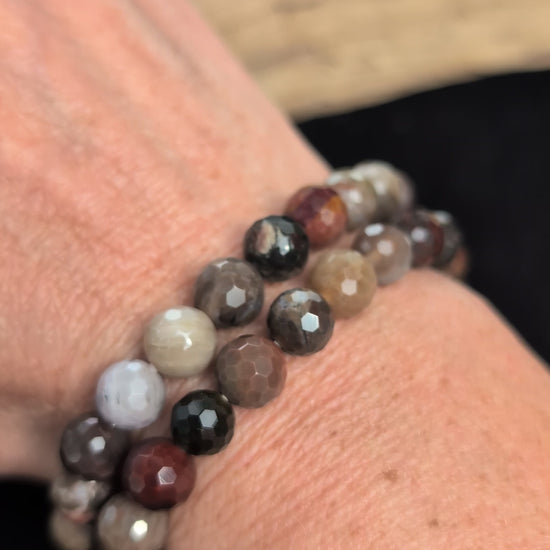 Video of 8mm faceted Petrified Wood beaded stretch bracelet resting on a driftwood display, showing earthy brown, grey, and tan fossil colouration.