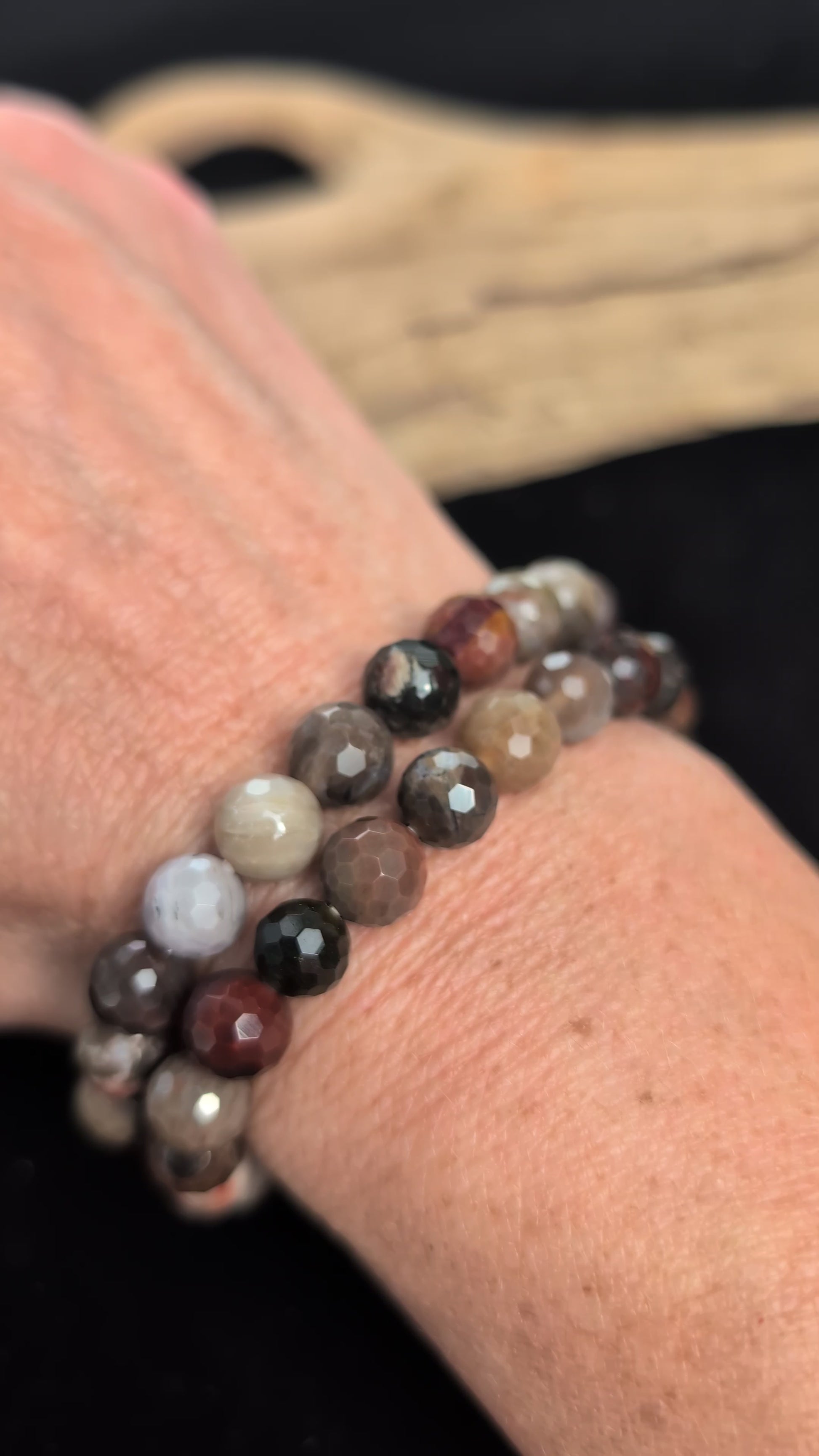 Video of 8mm faceted Petrified Wood beaded stretch bracelet resting on a driftwood display, showing earthy brown, grey, and tan fossil colouration.