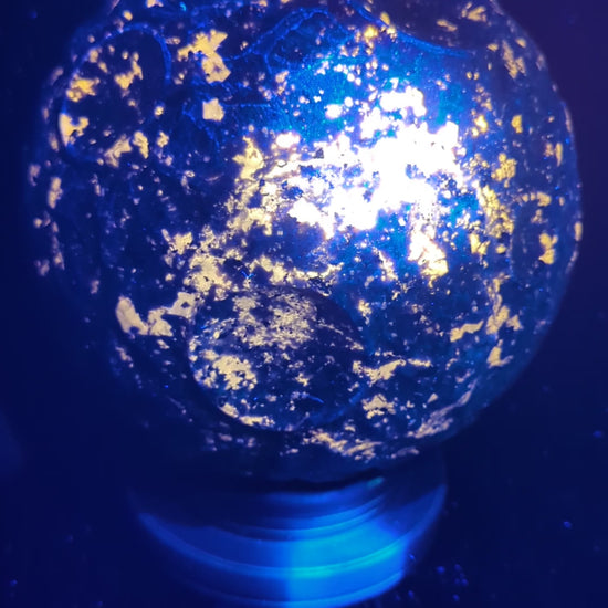 A massive 210 mm (8.27 in) Yooperlite carved moon sphere glowing intensely orange under UV light, highlighting natural sodalite inclusions.