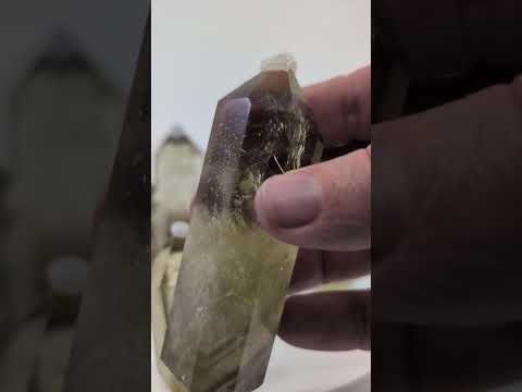A video tour of nine natural, polished Smoky Citrine towers from Brazil. The camera pans across the standing collection, and a hand picks up several individual pieces to showcase their striking bicolored zoning—from deep smoky quartz bases to pale golden-yellow tips. Close-up shots reveal excellent internal clarity, natural fracture planes creating iridescent rainbows, and dark, floating mineral inclusions suspended within the polished quartz.