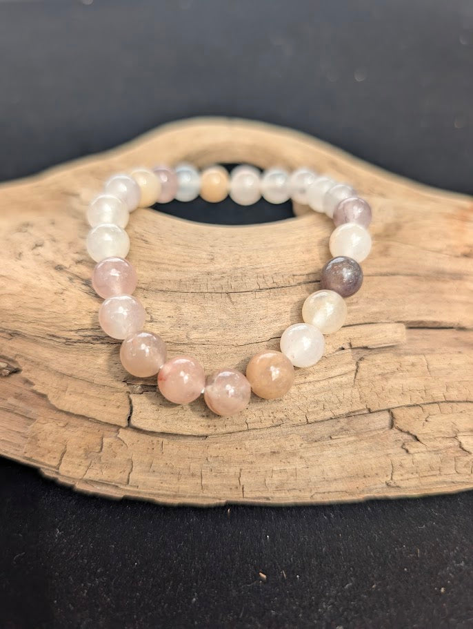 An 8mm Purple Aventurine beaded bracelet resting on natural driftwood, displaying translucent, dusty lavender and milky white quartz colours.