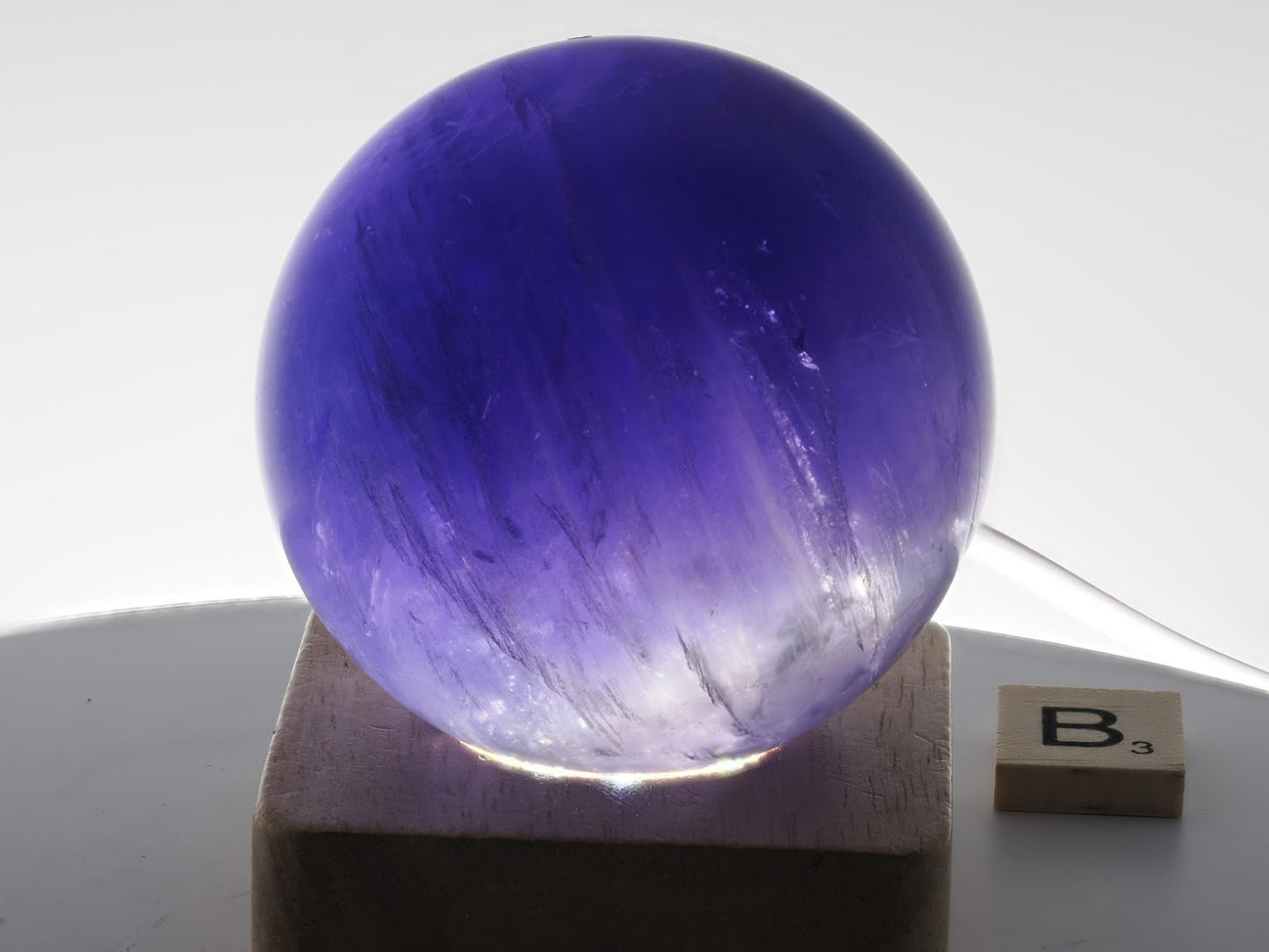 Full illumination of 64mm Purple Fluorite sphere specimen B highlighting royal plum tones.