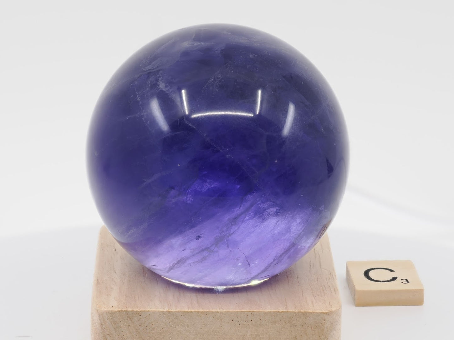 Translucent lilac and dark purple phantom chevrons inside a polished 69mm Fluorite sphere.