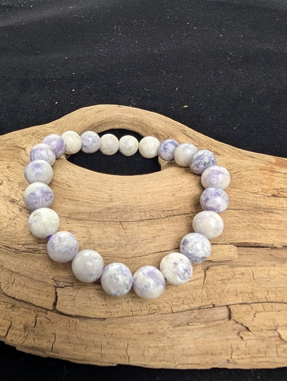8mm polished Purple Opal beaded stretch bracelet resting on a driftwood display, showing marbled violet and creamy white tones.