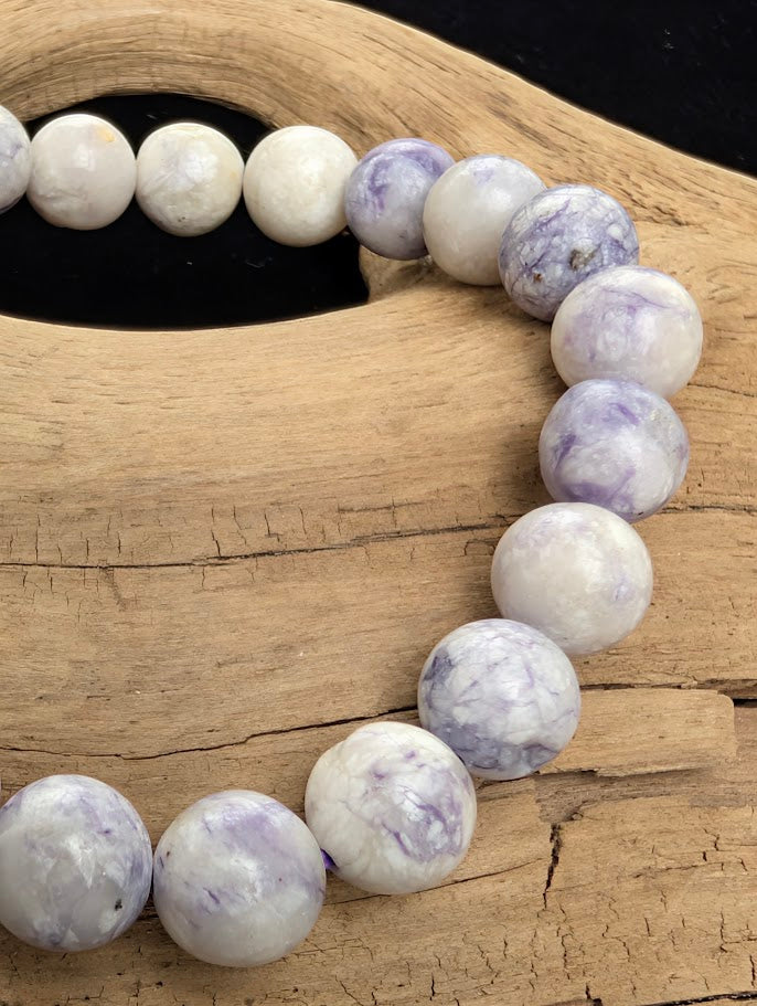 Macro close-up of 8mm polished Purple Opal beads highlighting the high-gloss finish and the natural purple and white silica marbling.