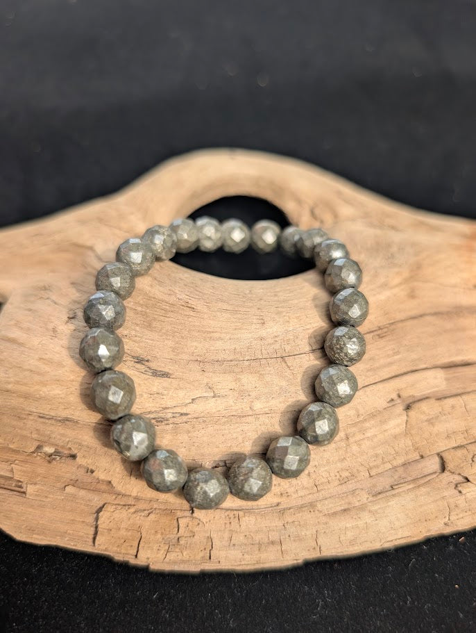 8mm faceted Pyrite beaded stretch bracelet resting on a driftwood display, showing a metallic brass-yellow lustre.