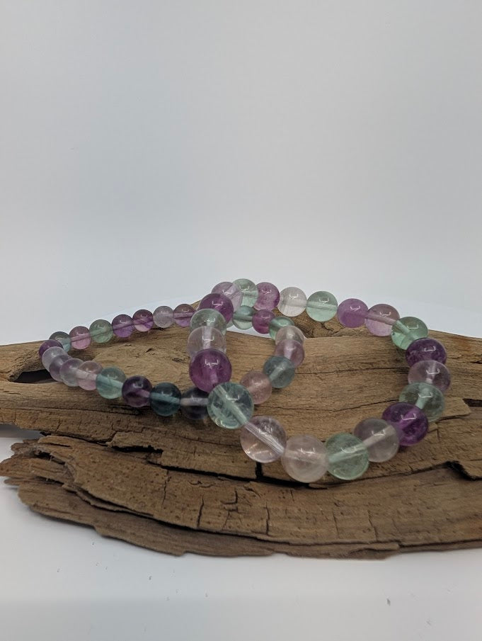 Two rainbow fluorite bracelets showing green, purple, pink and clear beads on driftwood