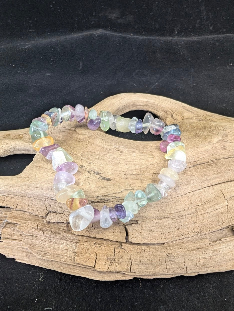 Full view of a Rainbow Fluorite chip bracelet on driftwood, showcasing a spectrum of purple, green, and translucent yellow-teal crystals.