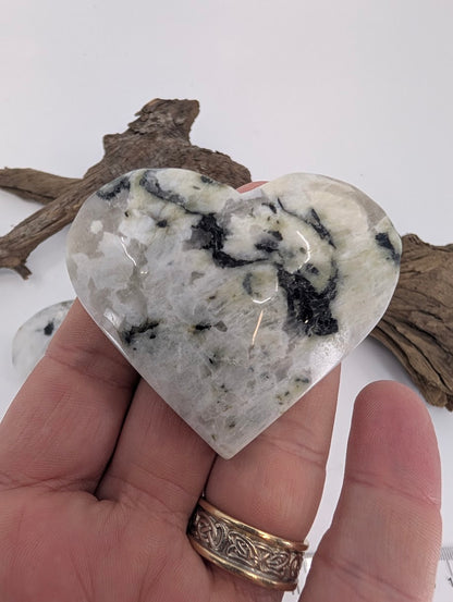 Hand holding a medium 100g Rainbow Moonstone heart.