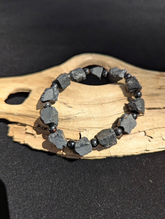 Raw Black Tourmaline stretch bracelet resting on a driftwood display, showing large rugged unpolished black chunks separated by smooth 6mm spherical spacer beads.