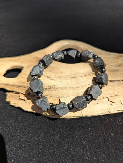 Raw Black Tourmaline stretch bracelet resting on a driftwood display, showing large rugged unpolished black chunks separated by smooth 6mm spherical spacer beads.