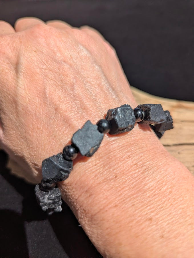 Raw Black Tourmaline stretch bracelet with large unpolished chunks and 6mm spacer beads worn on a wrist for size scale.