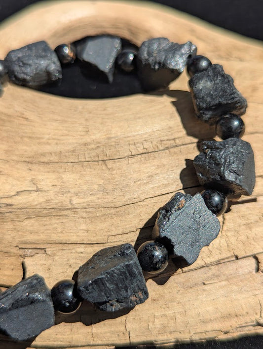 Macro close-up of large raw Black Tourmaline chunks highlighting the unpolished, natural texture and vertical crystalline striations next to smooth 6mm spacer beads.