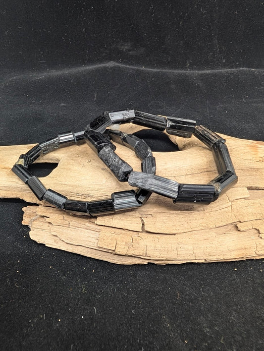 Two raw Black Tourmaline bar bracelets showing natural striations on a driftwood display.