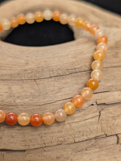 Macro view of polished 4mm Red Aventurine spherical beads on driftwood, highlighting the natural translucency and subtle internal hematite inclusions.