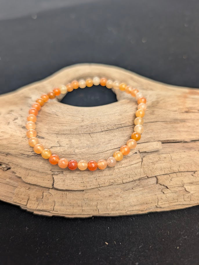 A 4mm Red Aventurine beaded bracelet resting on natural driftwood, displaying translucent peach to deep orange-red quartz colours.