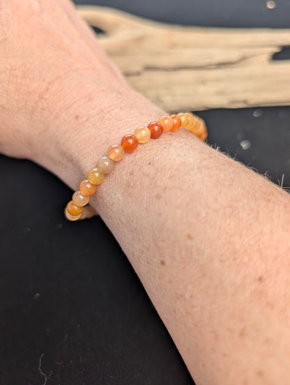 Natural sunlight on a 4mm warm orange-red Red Aventurine stretch bracelet worn on a wrist.