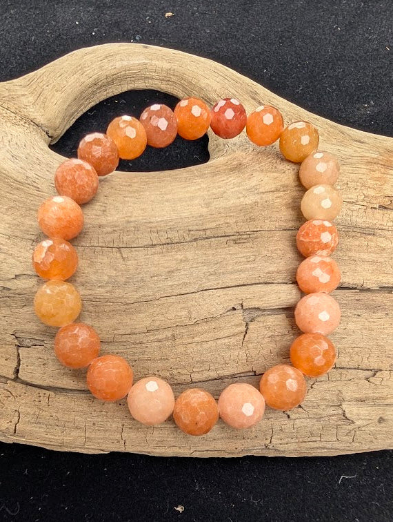 8mm faceted Red Aventurine stretch bracelet resting on a driftwood display, showing warm peach and terracotta tones.