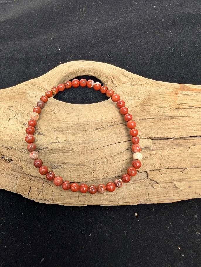 4mm polished Red Jasper beaded stretch bracelet resting on a driftwood display, showing earthy red and brecciated quartz patterns.