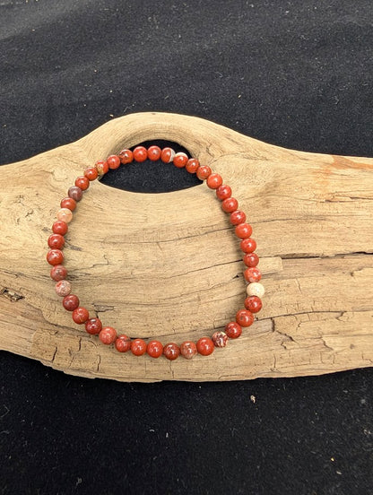 4mm polished Red Jasper beaded stretch bracelet resting on a driftwood display, showing earthy red and brecciated quartz patterns.