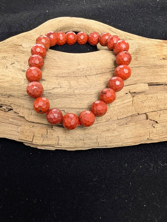8mm faceted Red Jasper beaded stretch bracelet resting on a driftwood display, showing earthy deep brick-red colouration.