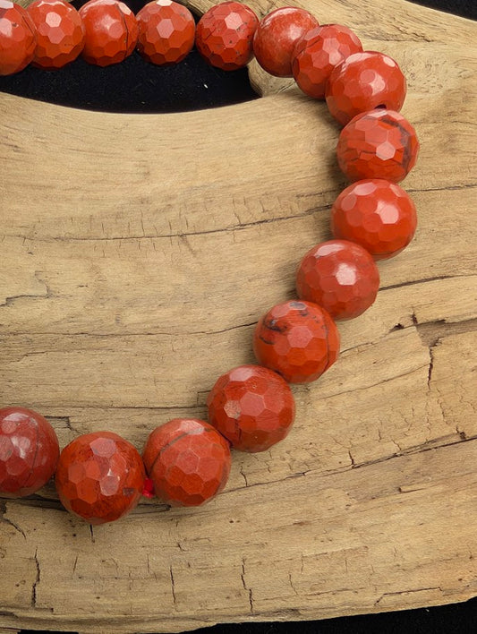 Macro close-up of 8mm faceted Red Jasper beads highlighting geometric surface cuts and a red stretch cord.