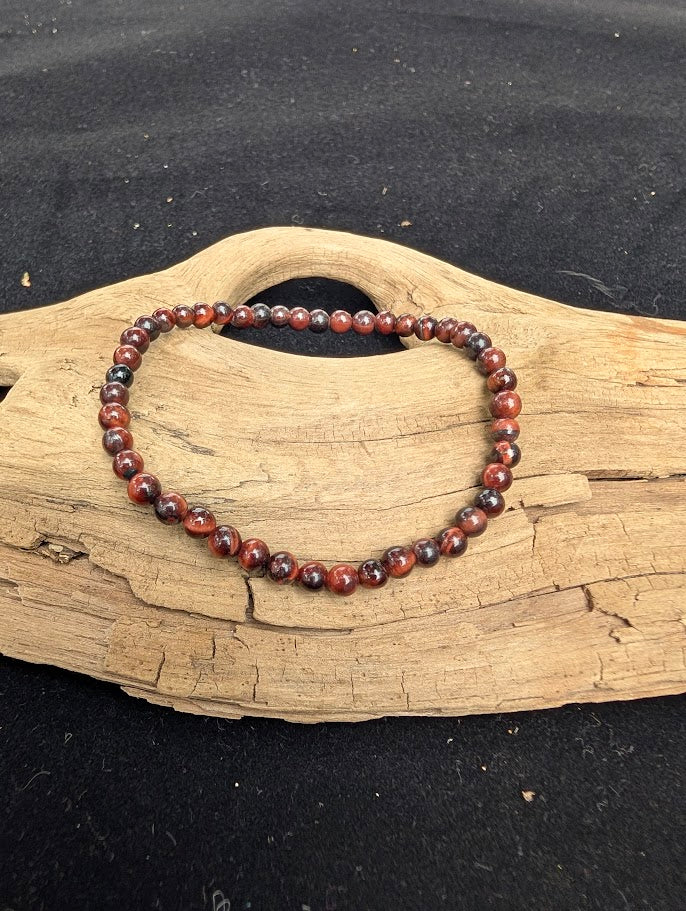 4mm polished Red Tiger Eye beaded stretch bracelet resting on a driftwood display, showing deep mahogany tones and natural chatoyancy.
