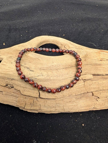 4mm polished Red Tiger Eye beaded stretch bracelet resting on a driftwood display, showing deep mahogany tones and natural chatoyancy.