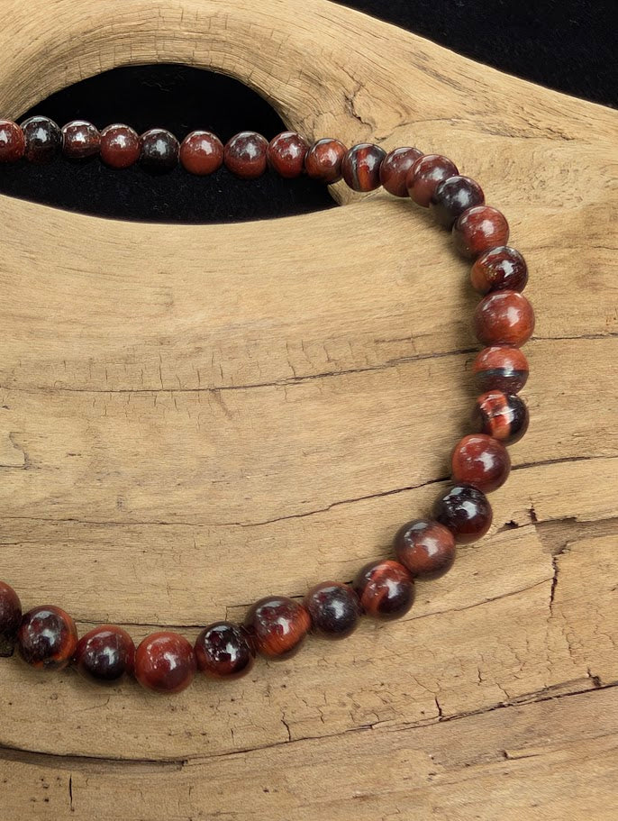 Macro close-up of 4mm polished Red Tiger Eye beads highlighting the high-gloss finish and the silky red chatoyant flash.