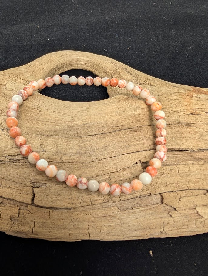4mm polished Red Vein Jasper beaded stretch bracelet resting on a driftwood display, showing a pale matrix with red hematite veining.