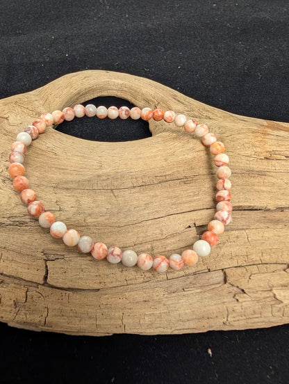 4mm polished Red Vein Jasper beaded stretch bracelet resting on a driftwood display, showing a pale matrix with red hematite veining.