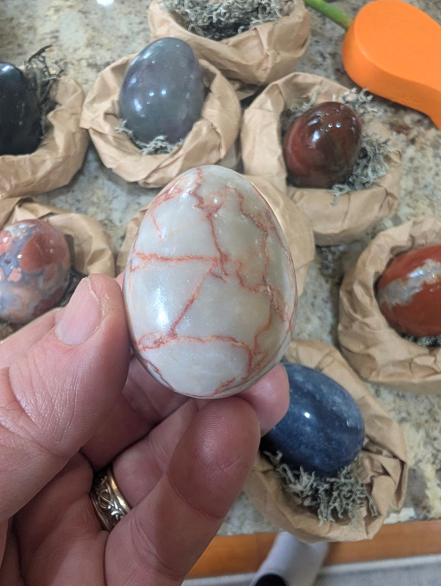A 2-inch polished Red Vein Jasper egg held in a hand, displaying striking red, grey, and white webbed veins across the natural stone surface.