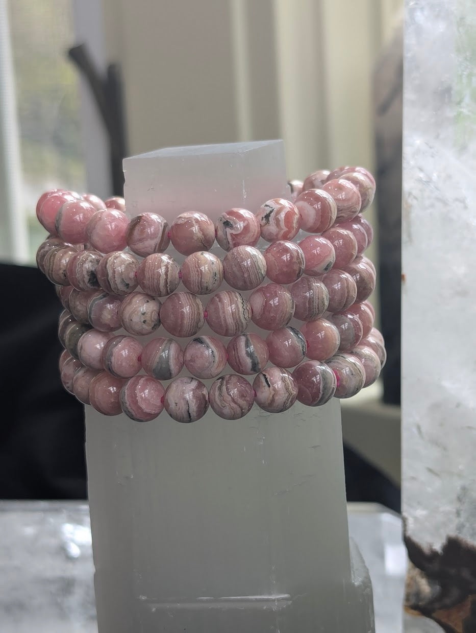 A stack of five 8mm Argentinian Rhodochrosite bracelets displayed on a white selenite tower to show batch consistency and banding.