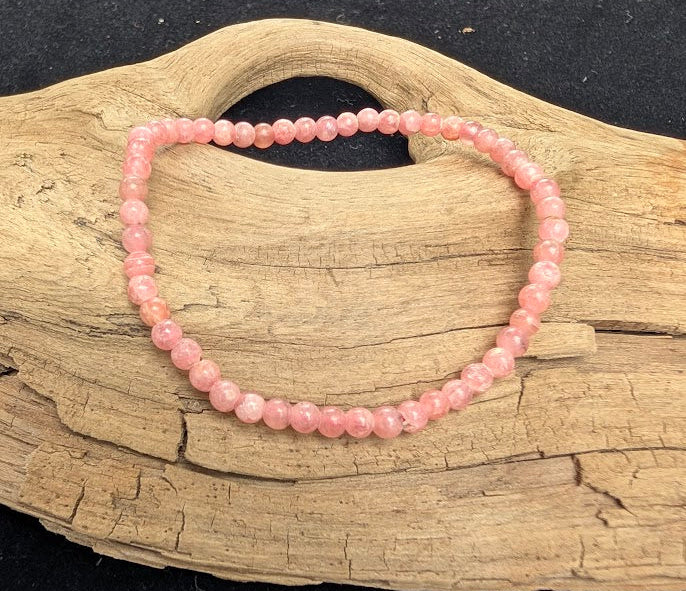 4mm AA-grade polished Rhodochrosite beaded stretch bracelet resting on a driftwood display, showing semi-translucent rose-pink tones and white banding.