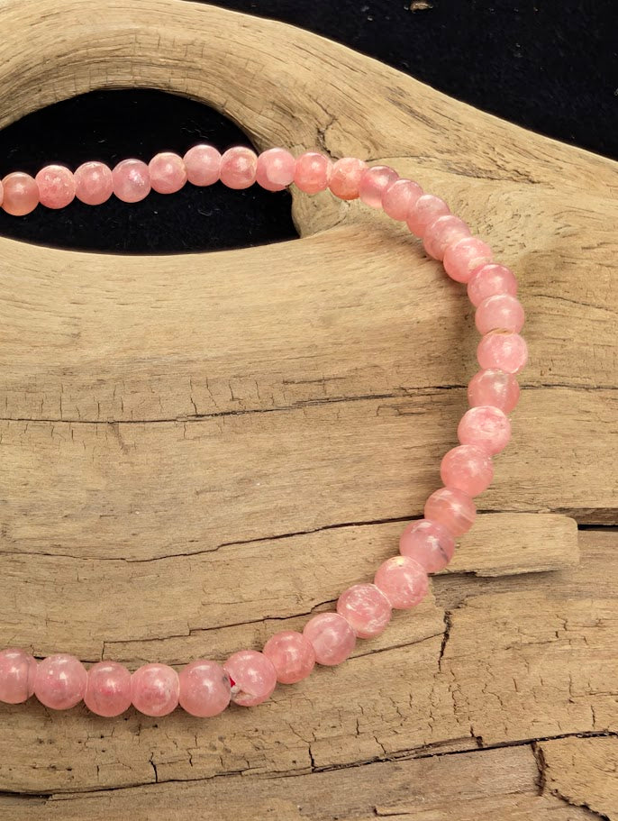 Macro close-up of 4mm AA-grade polished Rhodochrosite beads highlighting the high-gloss finish, deep pink colouration, and natural white calcite mottling.